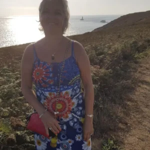 Simone Grunfelder, Accompagnatrice Holistique, souriante et apaisée, regardant l'océan au coucher du soleil, symbolisant le bien-être et l'équilibre